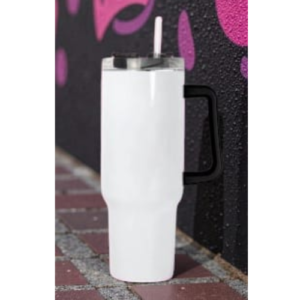 White reusable tumbler with a lid and straw, standing on a brick sidewalk beside a graffiti-covered wall.