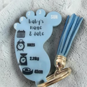 Blue baby footprint keychain displaying birth details (name, date, time, weight 2.3 kg, length 45 cm) with a tassel and icons for calendar and clock.