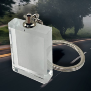 Clear rectangular crystal keychain with a metal ring on a blurred road background.