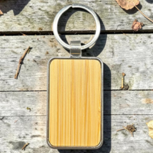 Rectangular wooden key tag with a metal frame and round key ring, lying on a weathered wooden surface.