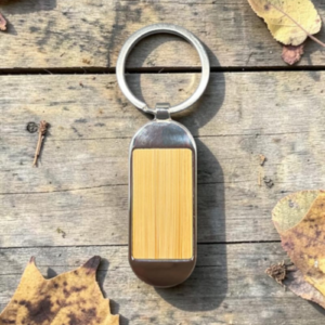 USB flash drive with a wooden center attached to a metal keyring, resting on a weathered wooden surface with autumn leaves nearby.