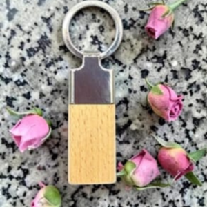 Wooden USB flash drive with a metal cap and ring, lying on speckled granite, surrounded by pink rosebuds.