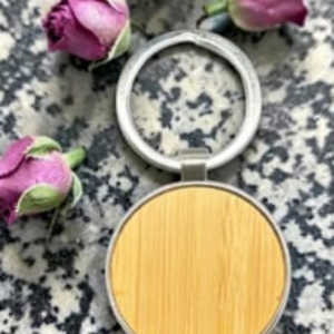Round wooden compact with a metal hinge open on a speckled granite surface, surrounded by pink rose buds.