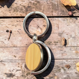 Top-down view of a metal keyring with a wooden oval pendant on a weathered wooden surface.