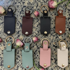 Colorful leather key fobs with metal rings arranged in two rows on a speckled surface, with pink roses nearby.