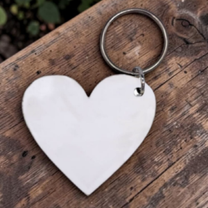 White heart-shaped keychain with metal ring resting on a weathered wooden surface
