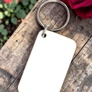 Metal key ring with a blank white rectangular tag lying on weathered wood, a red rose partially in the frame.
