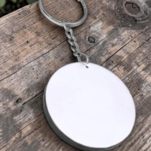 Round blank metal key tag attached to a key ring on a weathered wooden surface.