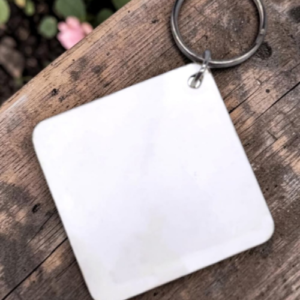 Blank white square keychain tag attached to a metal ring on a wooden surface