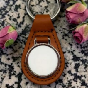 Brown leather keychain with a round metal watch case on a speckled surface, surrounded by pink rose petals.