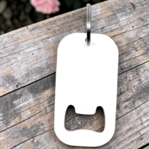 White plastic bottle opener with a metal key ring, resting on a weathered wooden surface. It has a curved body with a U-shaped opening at the bottom edge.