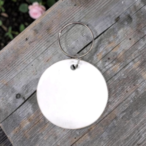 Round white blank key tag attached to a metal ring on a weathered wooden surface