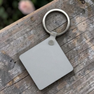 Blank gray square key tag attached to a metal ring on a weathered wooden surface, seen from above.