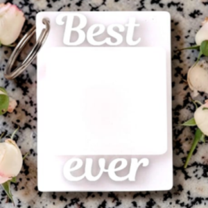 Decorative white card reading 'Best' at the top and 'ever' at the bottom with a blank square in the middle, on a speckled surface with pink roses and a metal binder ring visible.