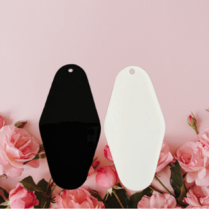 Two teardrop-shaped color swatches (one black, one white) with holes at the top, standing upright on a pink background with roses in the foreground.