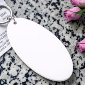 Blank white oval tag on a key ring resting on speckled granite with pink roses nearby