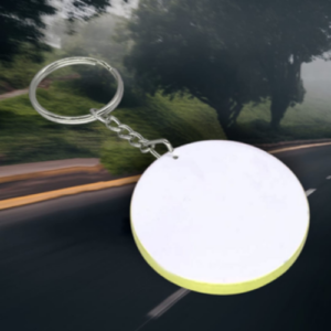 Round white keychain tag with a yellow rim hanging from a metal ring, blurred road background.