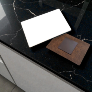 Two rectangular blocks sit on a dark, veined countertop: a white block and a brown corkboard with a small dark square inset.