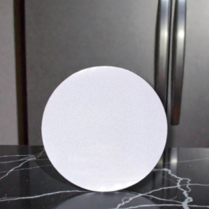 White circular disc standing on a dark marble kitchen counter, with a stainless steel refrigerator door in the background.