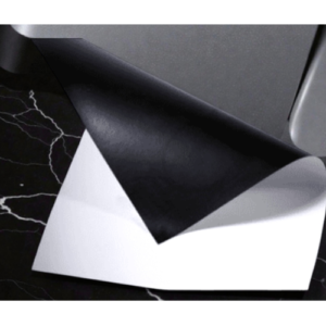 Two sheets of paper, one black on top of a white sheet, folded near the corner on a dark marble surface.