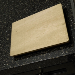 Beige rectangular cutting board resting on a dark speckled kitchen counter.